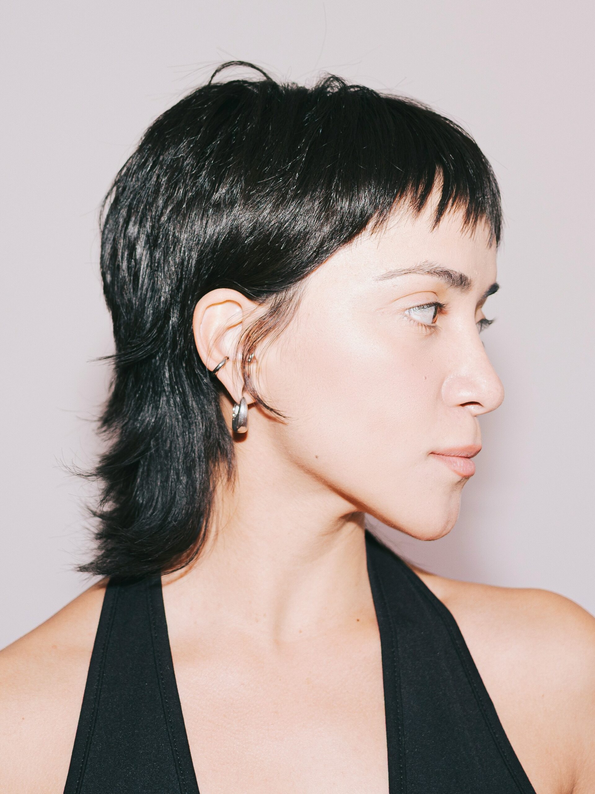 Een jonge vrouw met een strak mullet-kapsel in een zwarte haltertop.