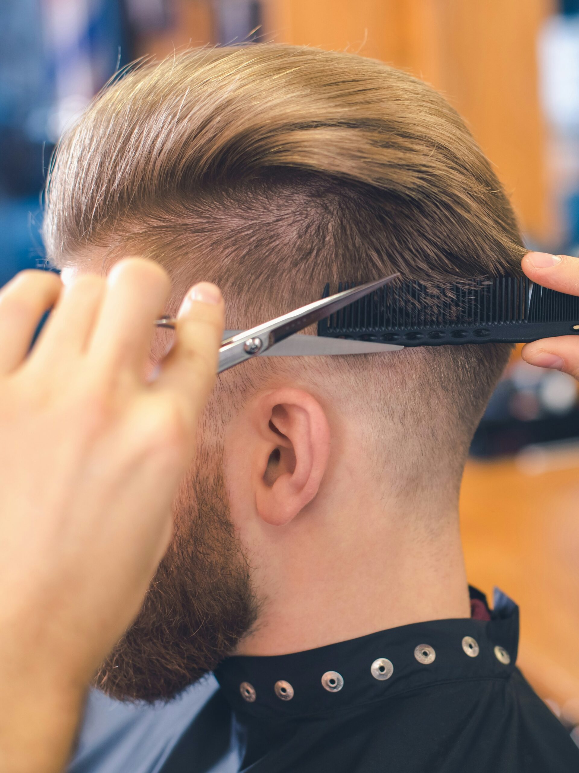 Close-up van een kapper die een taper fade knipt bij een klant met de schaar-over-kam techniek aan de achterkant van het hoofd