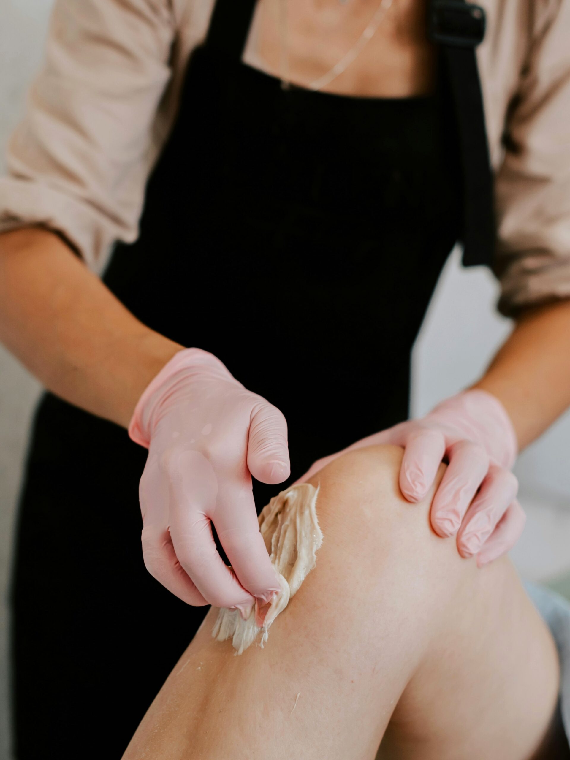 Zijaanzicht van een specialist die wax aanbrengt op het been van een cliënt, liggend op een behandelbed in de salon