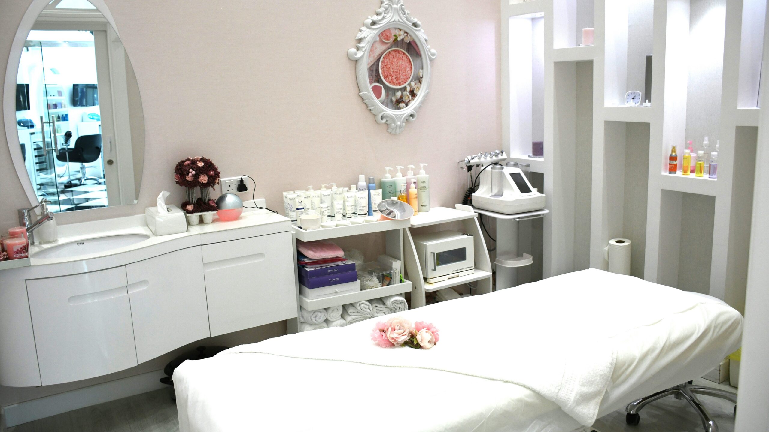 Lichte, schone en uitnodigende behandelkamer in een salon met een behandelbed, producten op planken, een sierlijke spiegel en bloemen