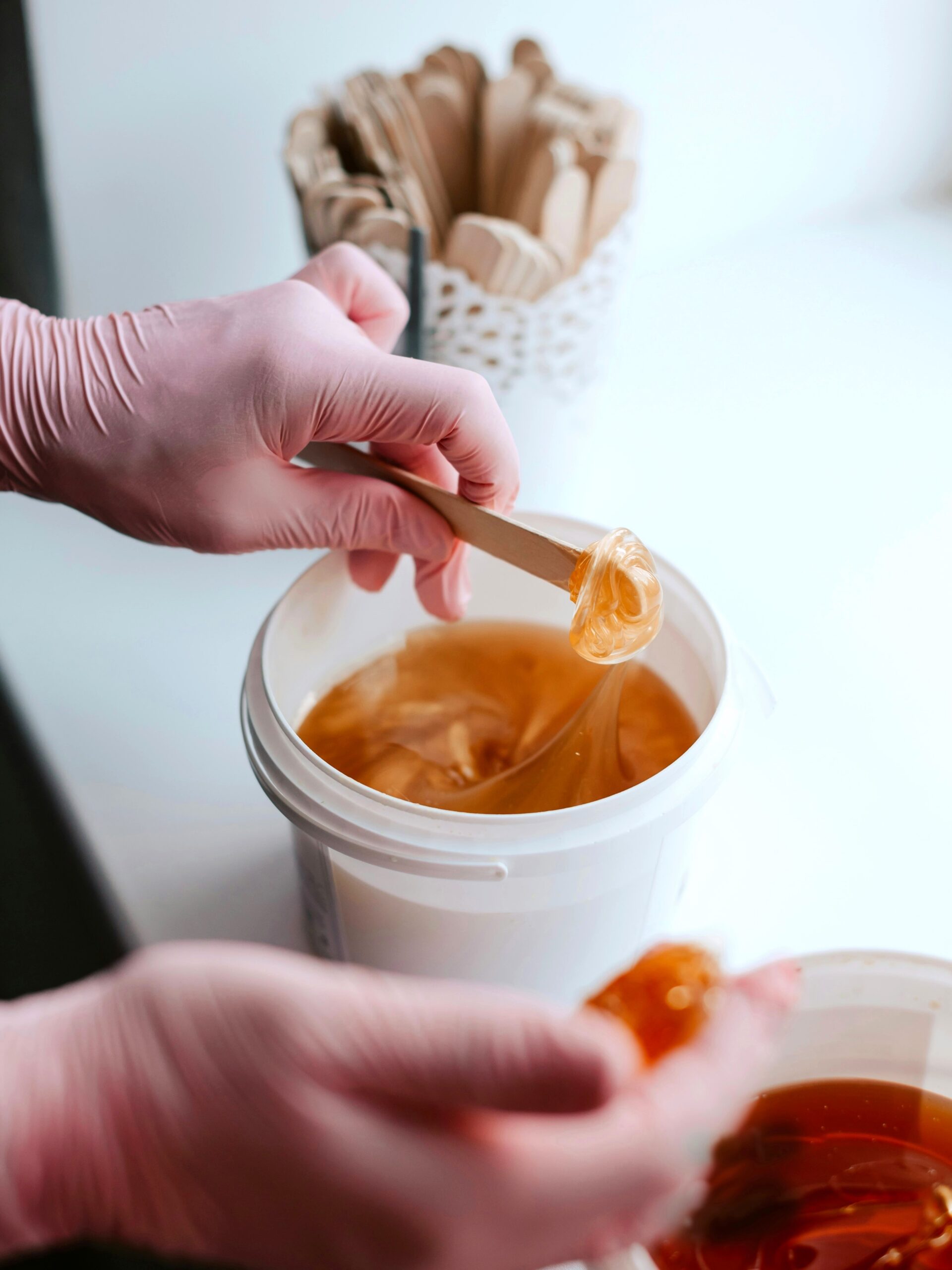 Close-up van twee potjes suikerwax terwijl een specialist wax opschept met een spatel