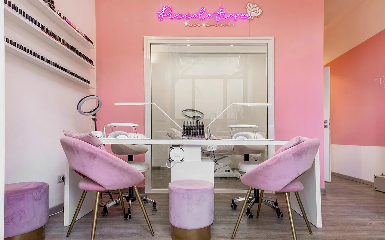 Een levendige manicurestation met felroze muren en een hot pink neonbord. Lila fluwelen stoelen met gouden poten staan bij een minimalistisch wit bureau uitgerust met professionele LED-nagellampen.