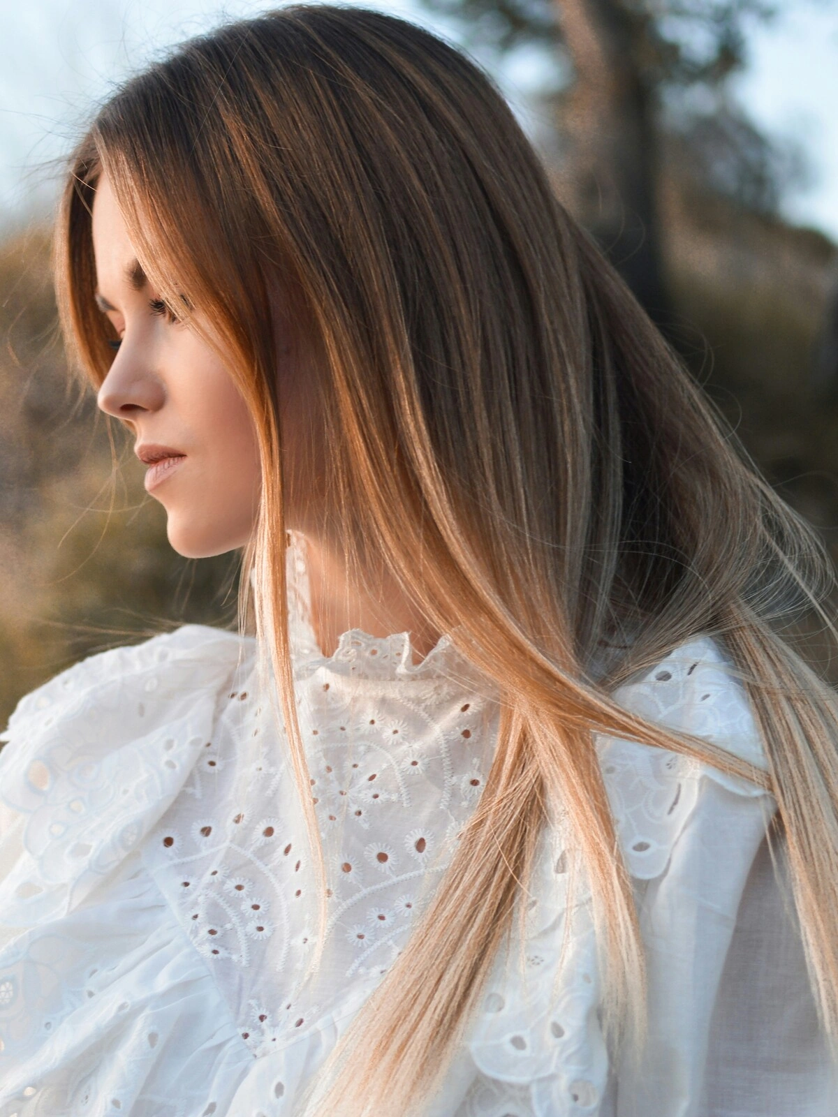 Zijaanzicht van een vrouw buiten in een natuurlijke omgeving, met balayage op steil haar waarbij het bruin overloopt in blonde tinten