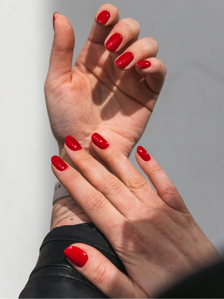 Close-up van de onderarmen van een vrouw in een zwart leren jasje, met een glanzende rode gelmanicure