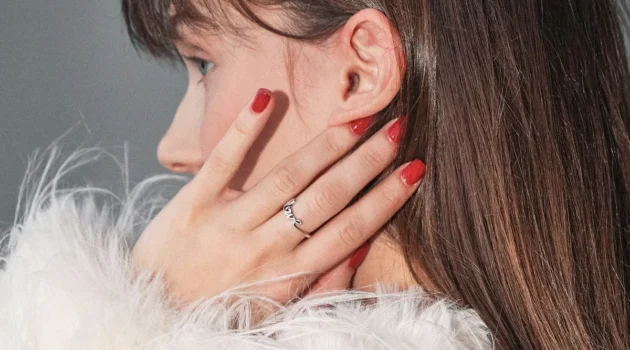 Close-up zijaanzicht van een brunette vrouw, met haar hand tegen haar gezicht en een glanzende rode gelmanicure