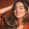 Close-up van een glimlachende vrouw met gesloten ogen die met haar handen door haar zachte, lange, donkerbruine haar gaat