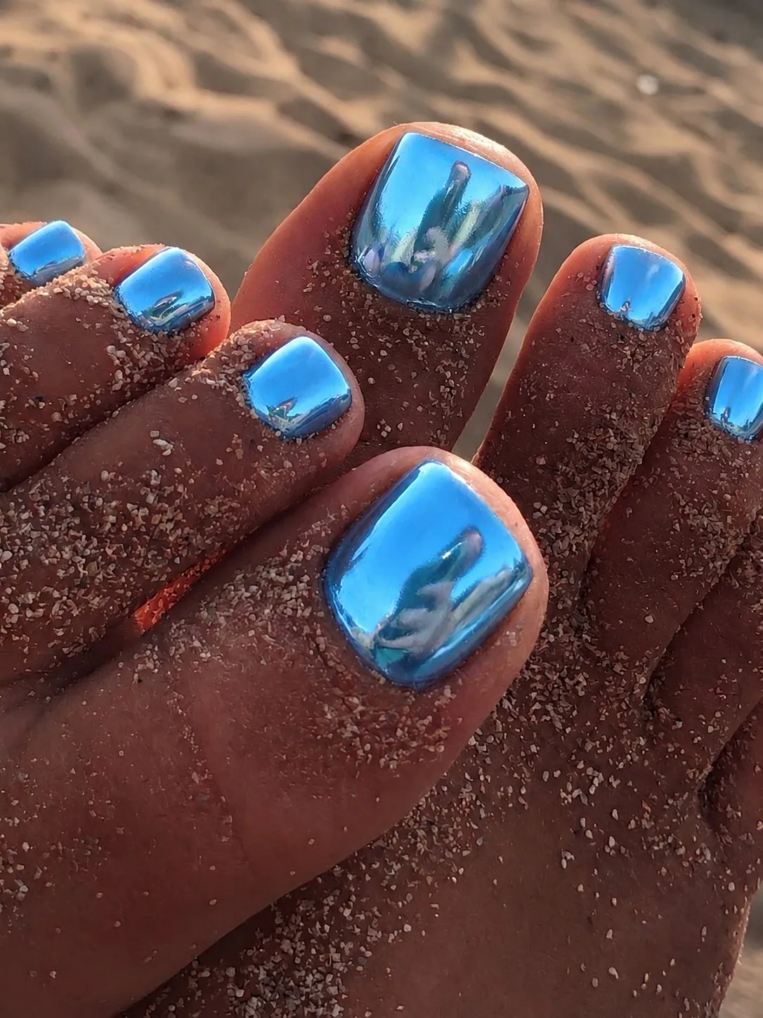 Metallic oceaanblauwe chrome pedicure op zandige voeten op het strand