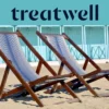 Twee gestreepte houten ligstoelen op het zand voor pastelblauwe strandhuisjes aan de kust van Versilia