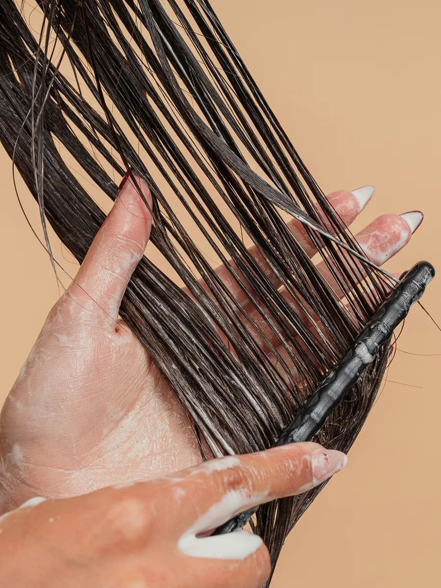 Close-up van een vrouw die conditioner door haar lange haar verdeelt met een grove kam