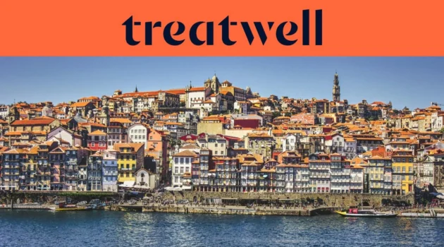 De Ribeira-kade in Porto, met rijen kleurrijke huizen en terracotta daken die vanaf de rivier de Douro tegen de heuvel op lopen, en de Clérigos-toren aan de horizon onder een strakblauwe lucht.