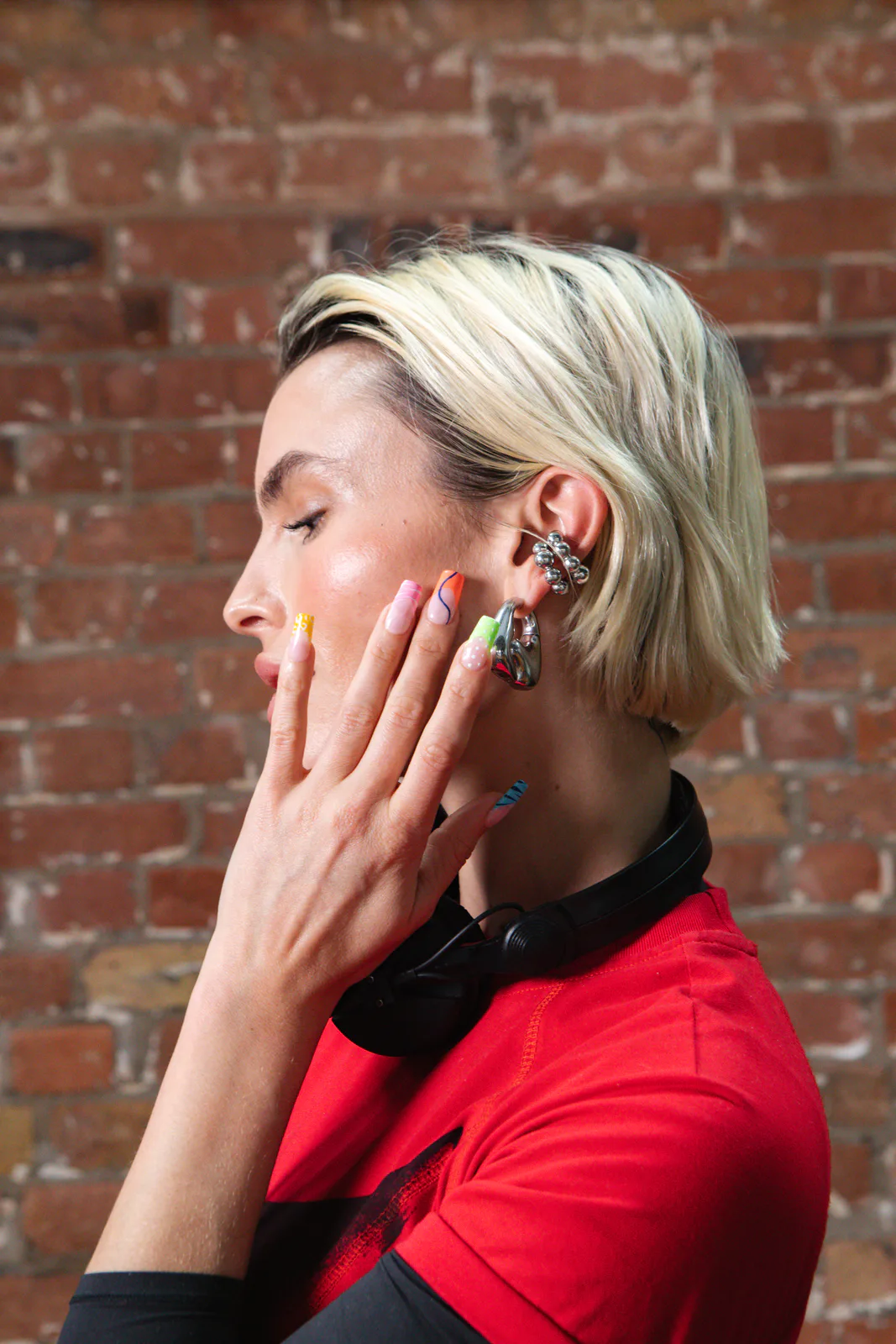 Dj en actrice Rex Adams van opzij, met de koptelefoon om de nek, terwijl ze de neon french tips van de kleurrijke electric mani laat zien