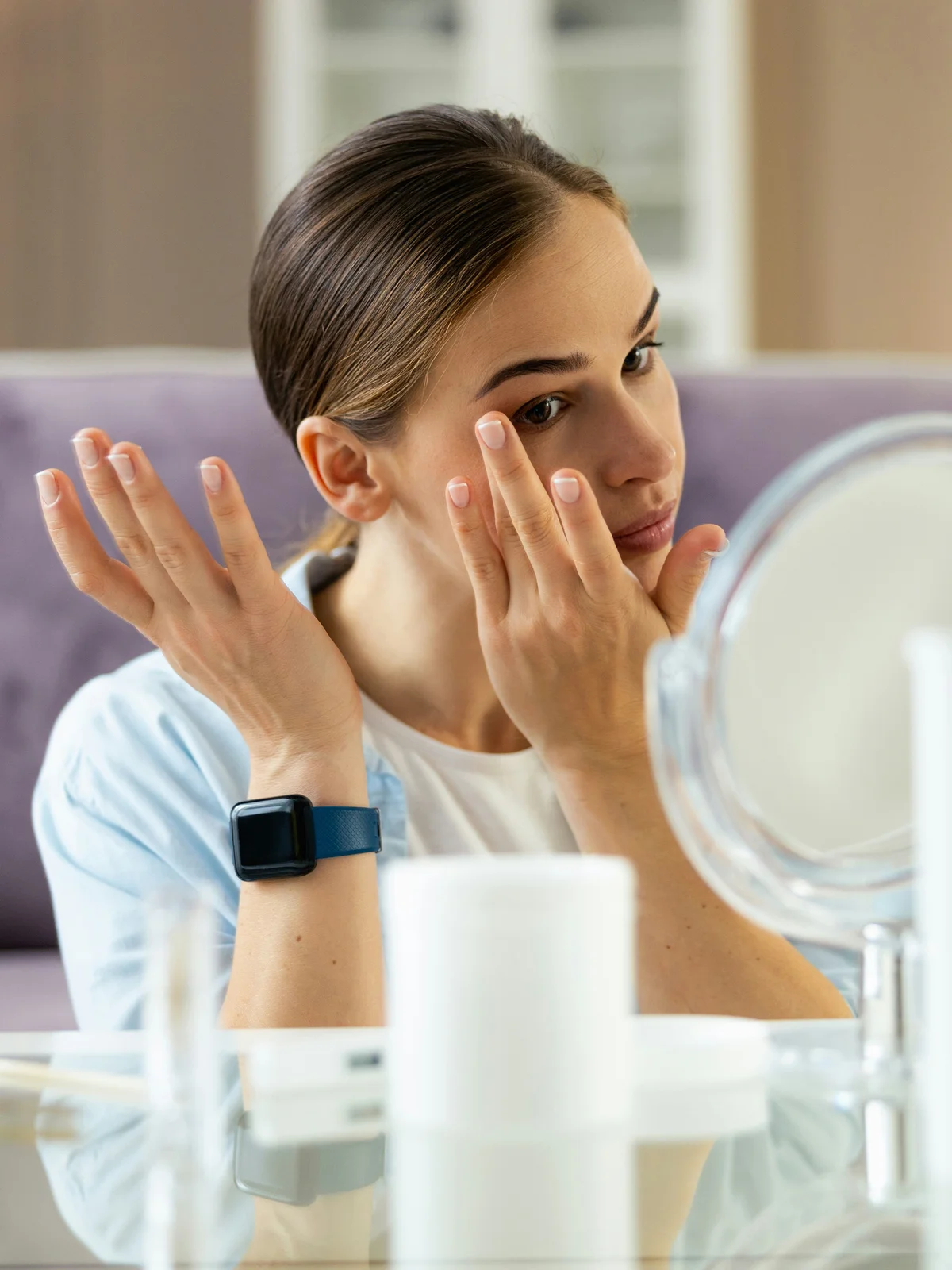 Een vrouw zit aan een tafel en brengt voorzichtig moisturizer en oliën aan op haar gezicht en wenkbrauwen