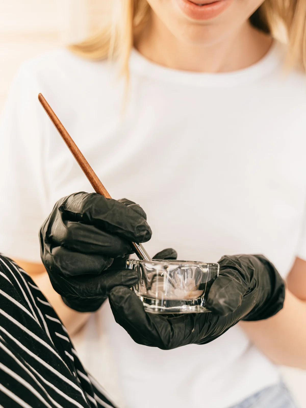 Close-up van een schoonheidsspecialiste met een klein glazen potje en een dun kwastje die wenkbrauwverf mengt in een salon
