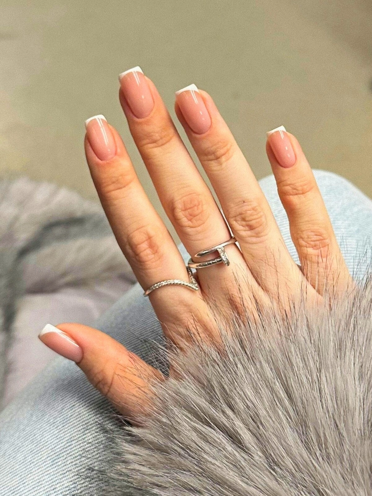De hand van een vrouw met een French manicure met microlijntjes op vierkante nagels
