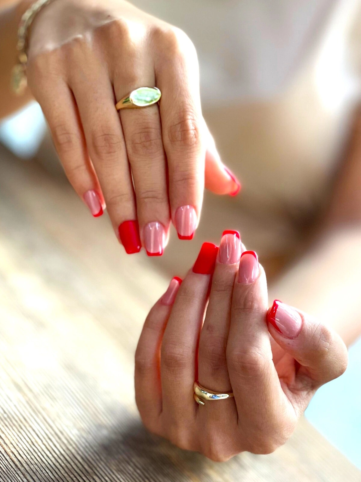 Een French manicure op vierkant-ovale nagels met een lichtroze basis en rode tips, en volledig rode ringvingernagels