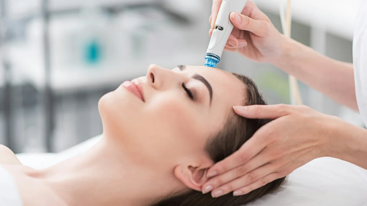 Close-up van een ontspannen vrouw met gesloten ogen tijdens een HydraFacial-behandeling in een rustige salon