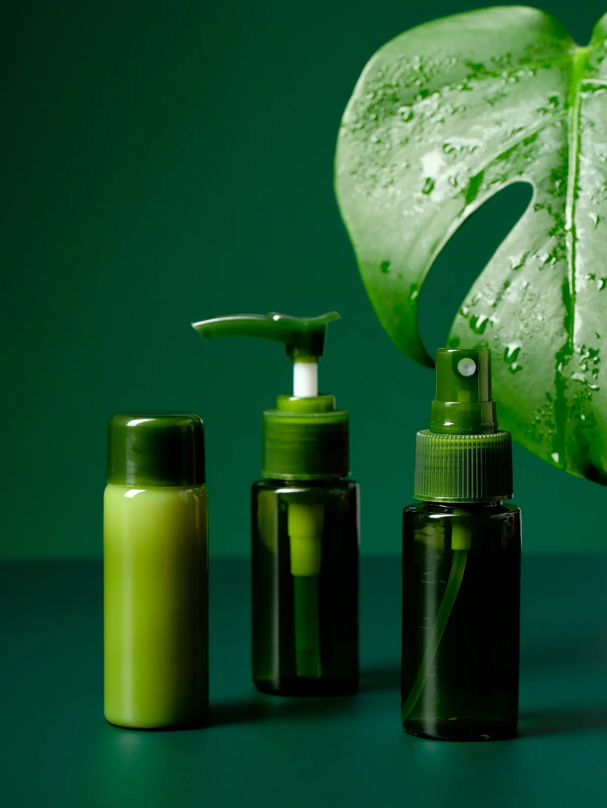 Productshot van drie kalmerende gels en crèmes in groene flesjes met een grote tropische groene bladvorm op de achtergrond