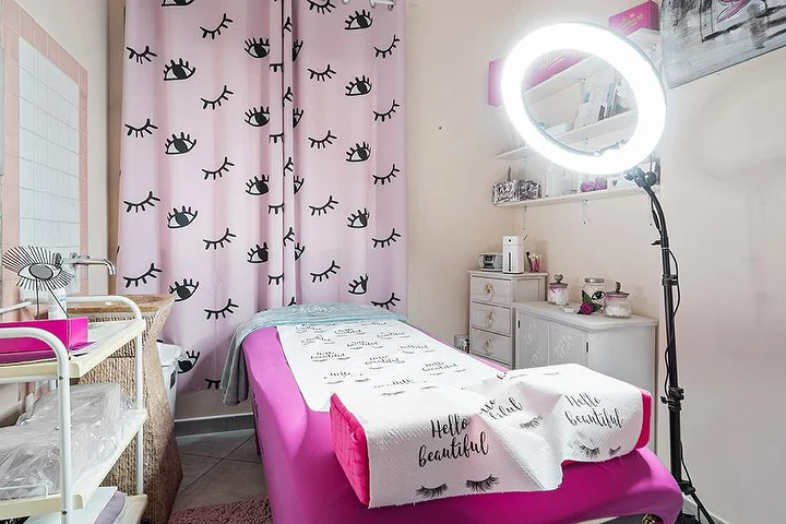 Roze behandelruimte bij Centro Estetico Karma in Olbia met wimperprint-gordijnen, beautybed en ringlamp.