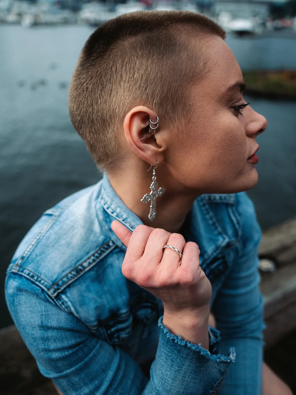 Bovenaanzicht van een vrouw met helix- en oorlelpiercings, zittend naast een rivier in een stad