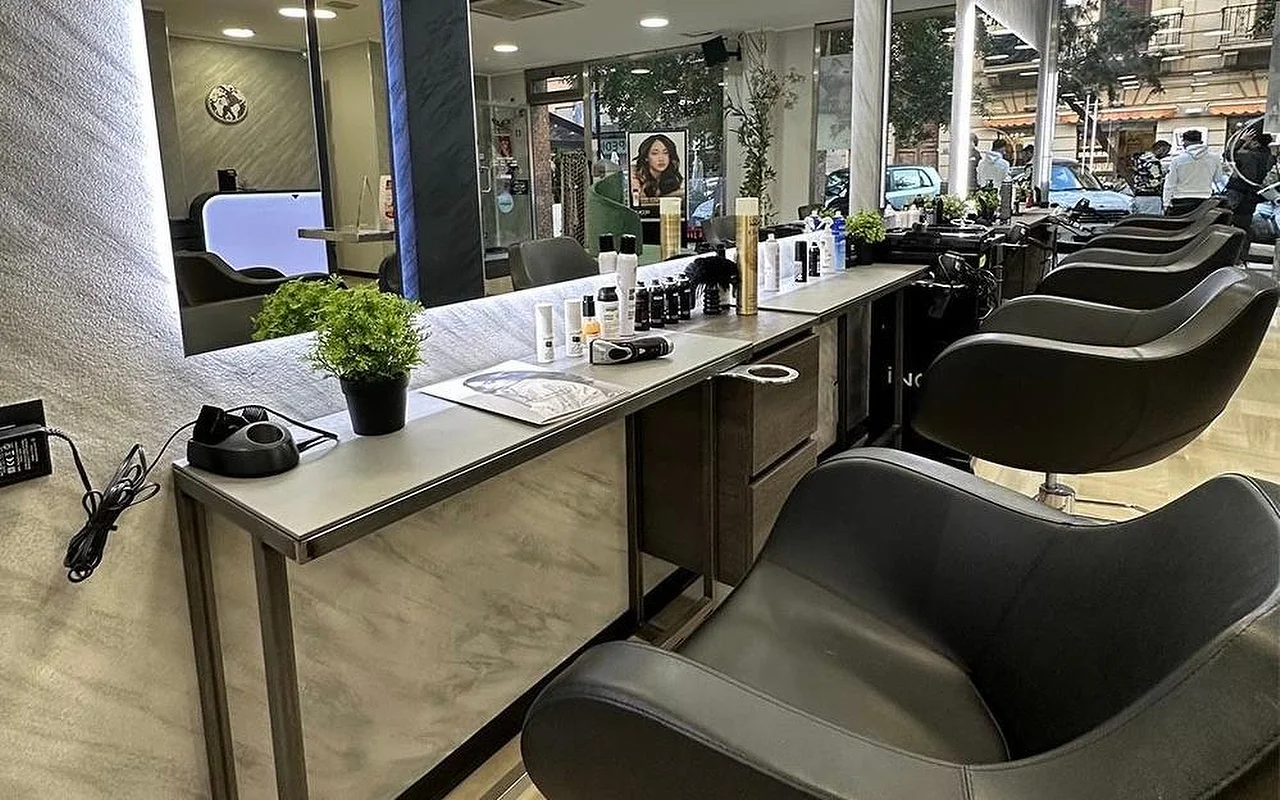 De stylingzone van Equipe Beauty, met een rij zwarte stoelen langs een balie met marmerlook, een grote verlichte spiegel, stylingproducten en een kamerplant op de balie, en vloer-tot-plafondramen op de straat.