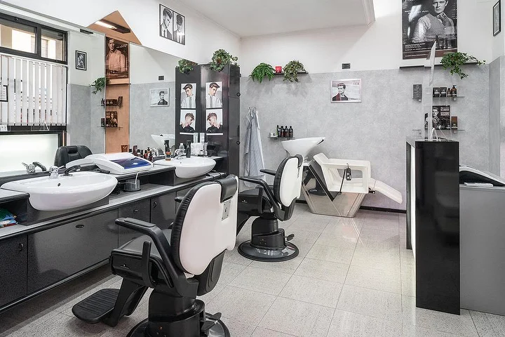 Vintage barberstoelen en wasplaatsen bij Fabio Desole Acconciature Maschili in Sassari met ingelijste portretten aan de muur.
