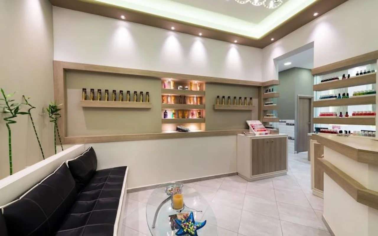 De crèmekleurige receptie van Fabulous Nails and More in Fira op Santorini, met een zwartleren bank, een glazen tafel, verlichte schappen met beautyproducten en zacht plafondlicht.