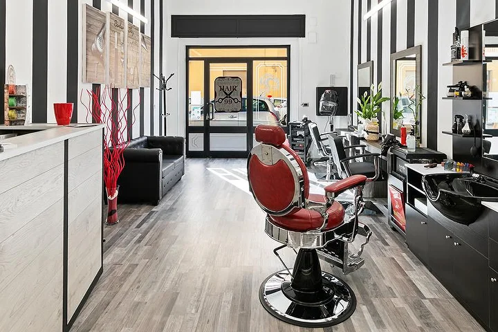 Rode vintage barberstoel bij Hair 99 in Alghero met de herkenbare zwart-witte streepmuren.