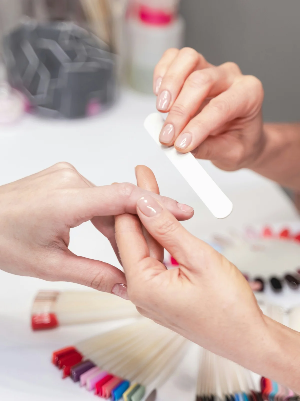 Close-up van een stylist die voorzichtig de nagels van een klant vijlt in een salon, met manicureproducten en materiaal op de achtergrond