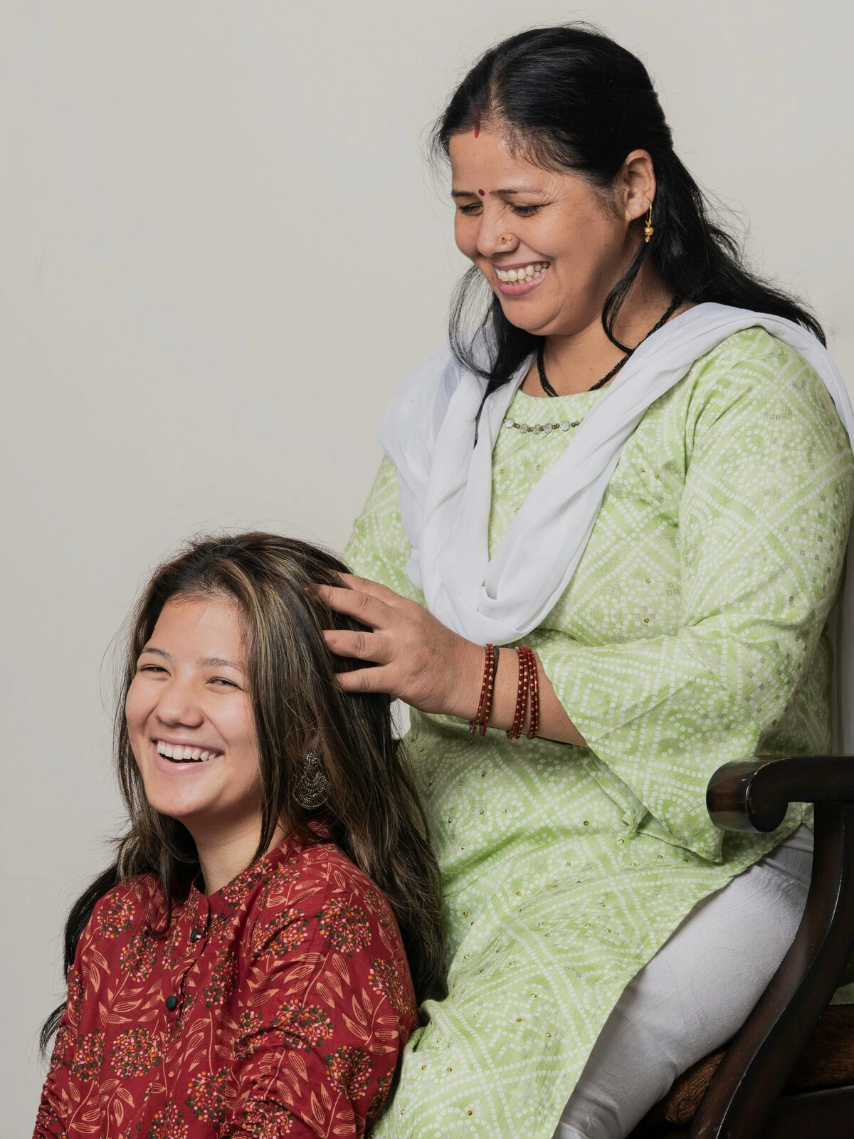 Een Indiase vrouw in traditionele kleding zit op een houten stoel en geeft een Indische hoofdmassage aan een vrouw die op de grond zit